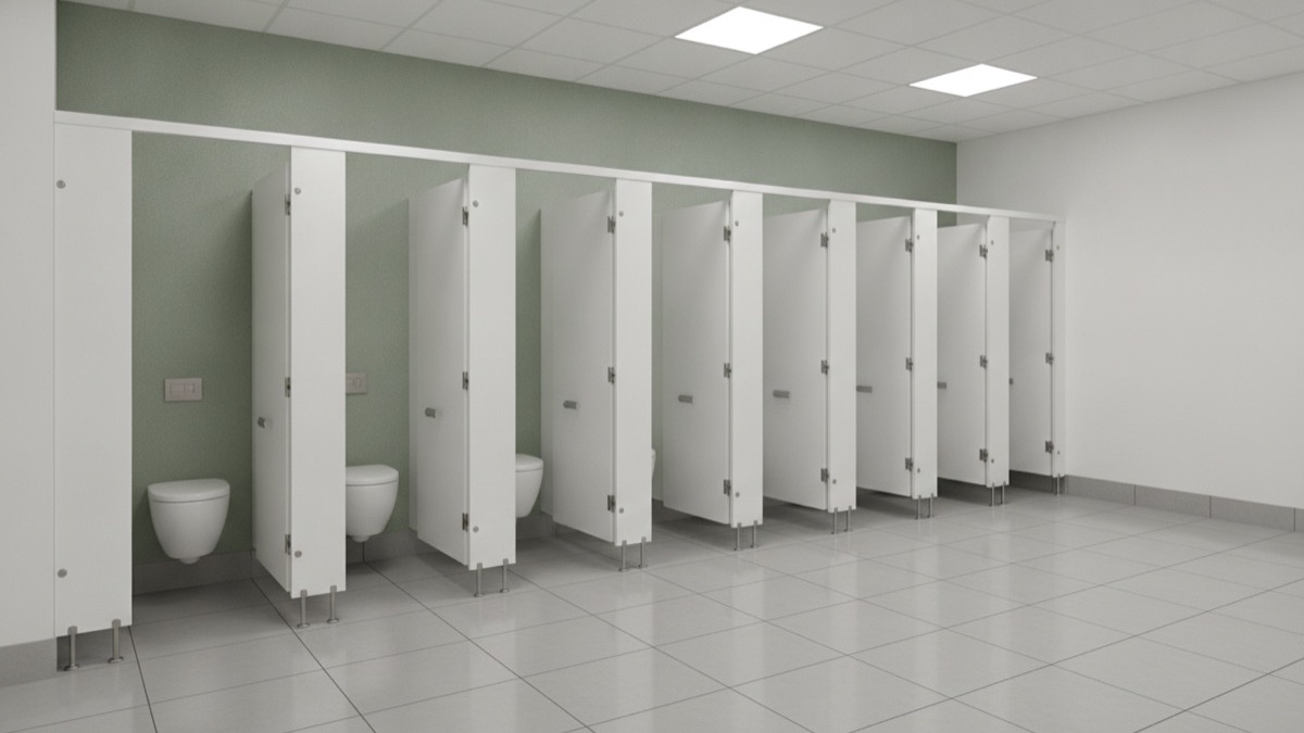 A spacious modern commercial washroom with several white cubicles, each with a wall-mounted sanitary bin